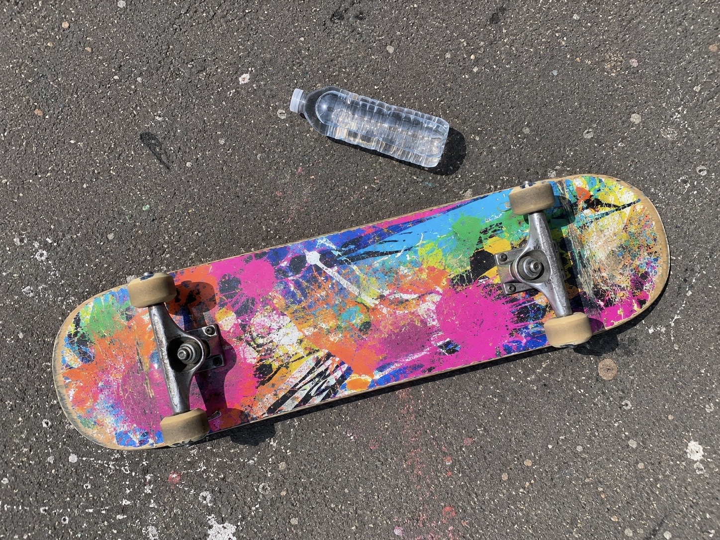 A splatter-painted skateboard resting on asphalt